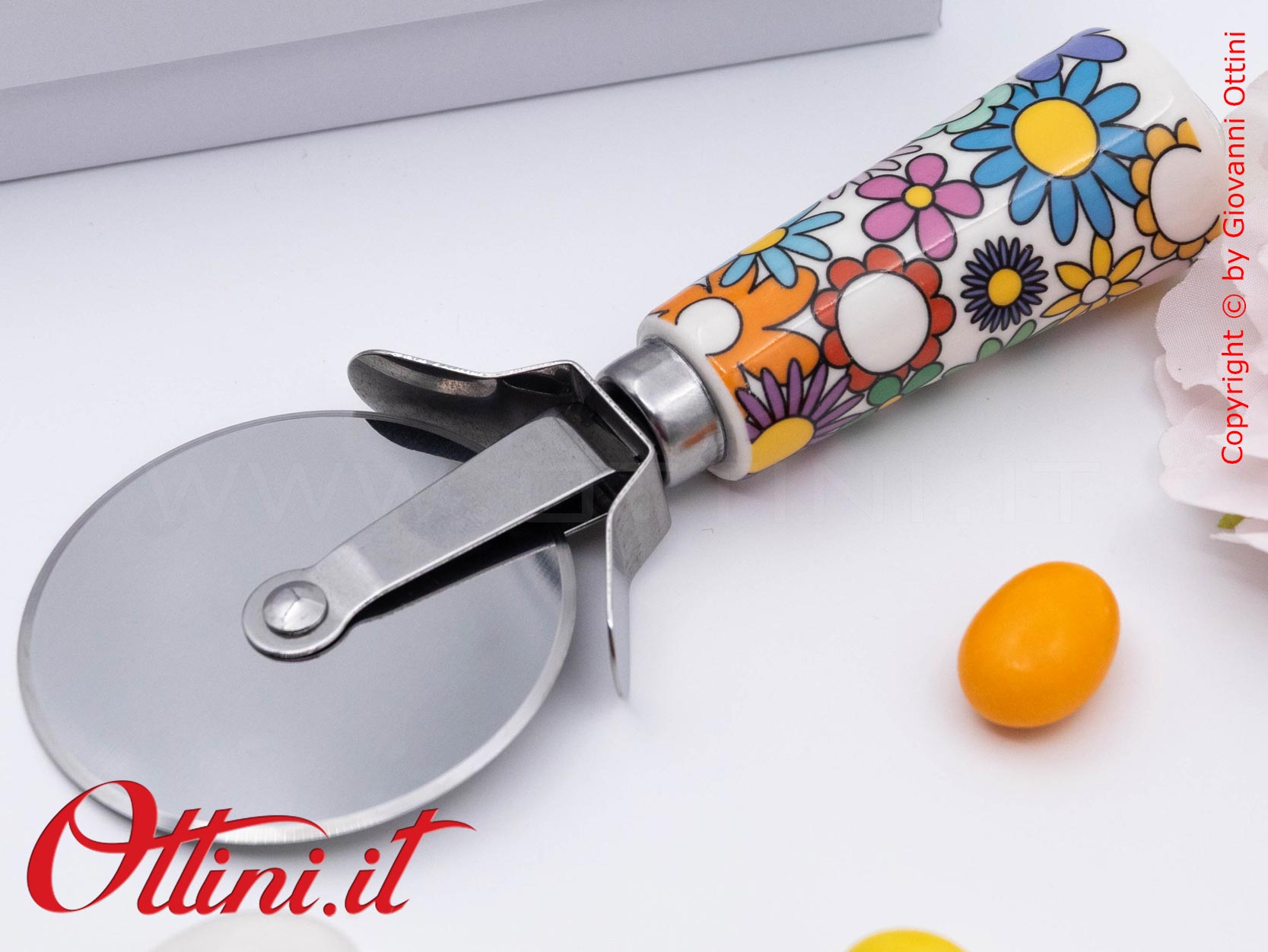DA202 - il Tagliapizza Fiorello di Cuorematto è una bomboniera solidale utile a tavola, caratterizzato da colori floreali vivaci e un design esclusivo
